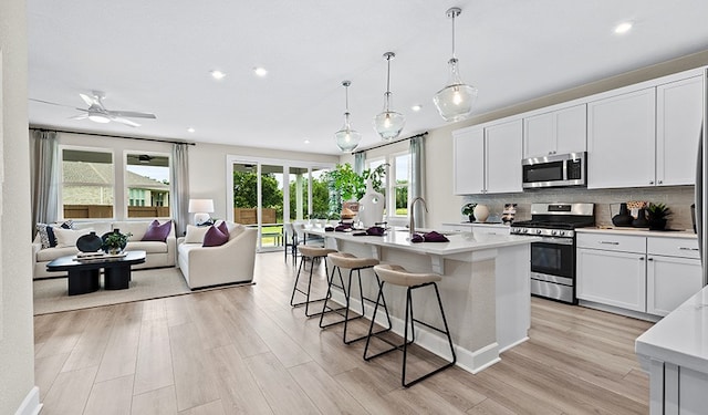 kitchen with appliances with stainless steel finishes, light hardwood / wood-style flooring, white cabinetry, and an island with sink