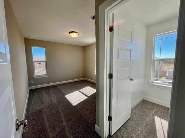 spare room with a wealth of natural light and dark carpet