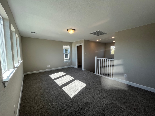 unfurnished room with dark colored carpet and a wealth of natural light