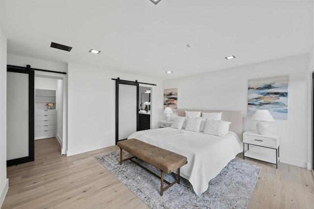 bedroom with a barn door and light wood-type flooring