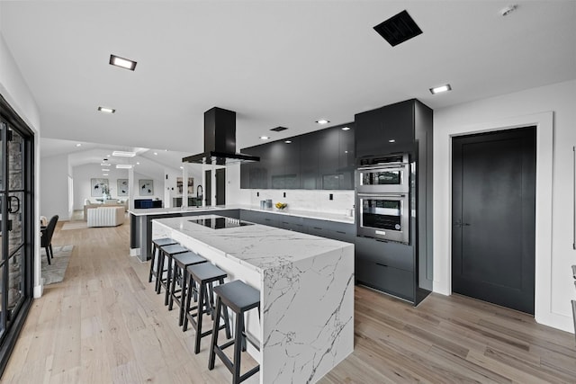 kitchen with a breakfast bar area, island range hood, light hardwood / wood-style flooring, double oven, and a center island