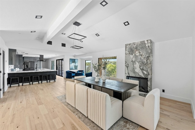 dining area with light hardwood / wood-style flooring, a fireplace, and lofted ceiling with beams