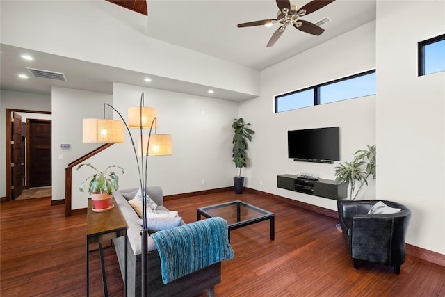 living room with a towering ceiling, ceiling fan, and dark hardwood / wood-style flooring