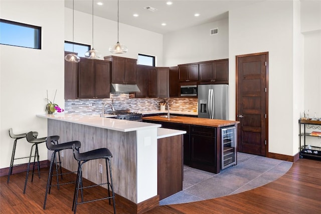 kitchen featuring kitchen peninsula, pendant lighting, stainless steel appliances, a breakfast bar area, and beverage cooler