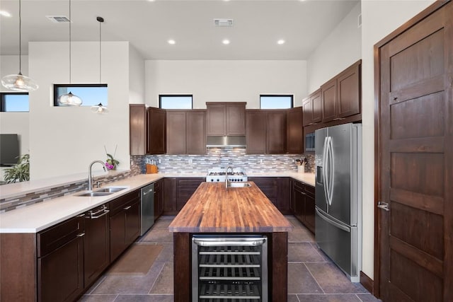 kitchen with sink, kitchen peninsula, pendant lighting, stainless steel appliances, and beverage cooler