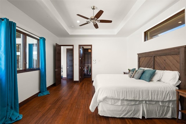 bedroom featuring ceiling fan, dark wood-type flooring, and a tray ceiling