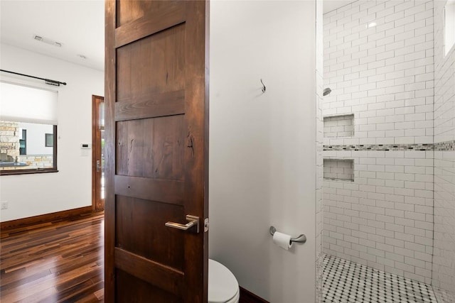 bathroom with hardwood / wood-style flooring, tiled shower, and toilet