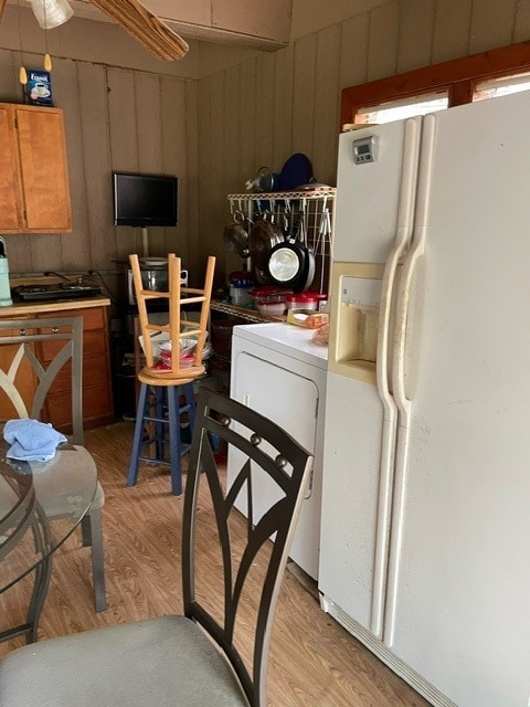 kitchen featuring wood walls, white refrigerator with ice dispenser, and light hardwood / wood-style flooring