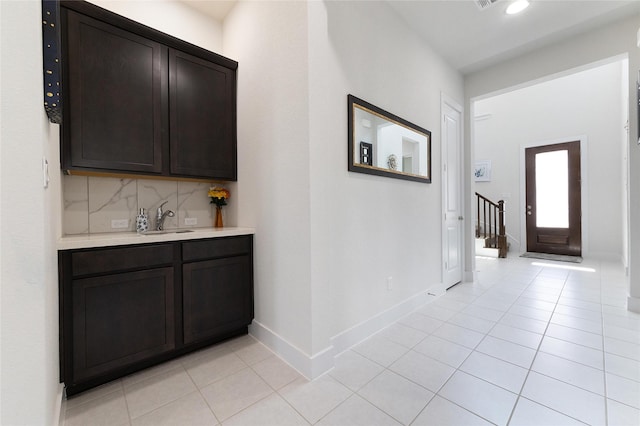 bar featuring sink, dark brown cabinets, light tile patterned flooring, and decorative backsplash