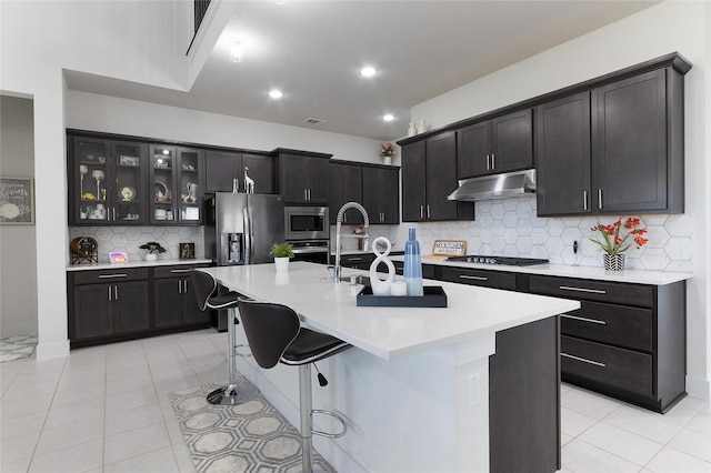 kitchen featuring tasteful backsplash, stainless steel appliances, light tile patterned flooring, and an island with sink