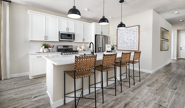 kitchen with an island with sink, a kitchen bar, white cabinetry, and appliances with stainless steel finishes