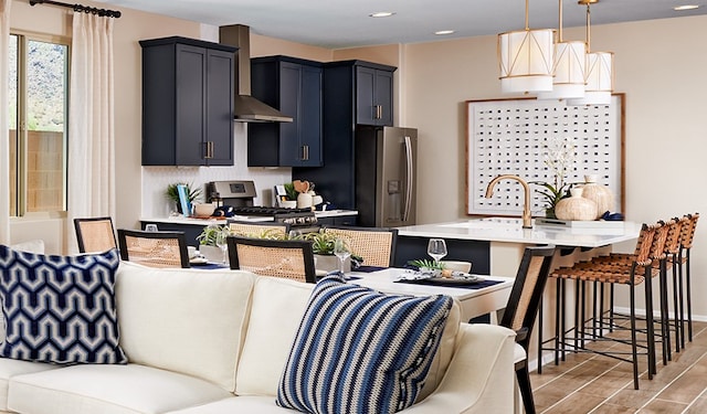 kitchen with wall chimney range hood, appliances with stainless steel finishes, light wood-type flooring, pendant lighting, and a kitchen breakfast bar