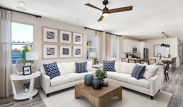 living room with a textured ceiling, ceiling fan, and light hardwood / wood-style flooring