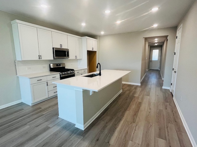 kitchen featuring white cabinets, light hardwood / wood-style flooring, sink, a kitchen island with sink, and appliances with stainless steel finishes