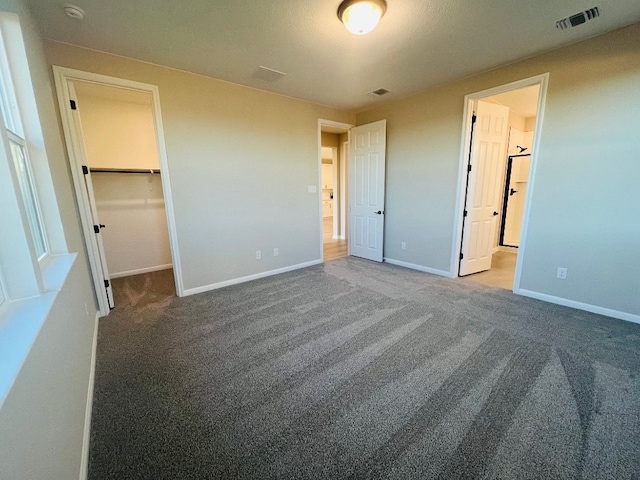 unfurnished bedroom with ensuite bath, a closet, a walk in closet, and carpet