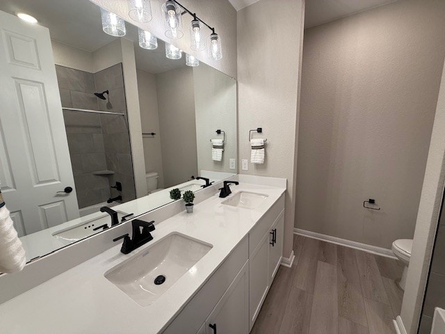 533 Raleigh Dr, Georgetown, TX 78633 - bathroom featuring toilet, wood finished floors, double vanity, a tile shower, and baseboards