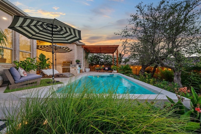 pool at dusk featuring an outdoor kitchen and a patio