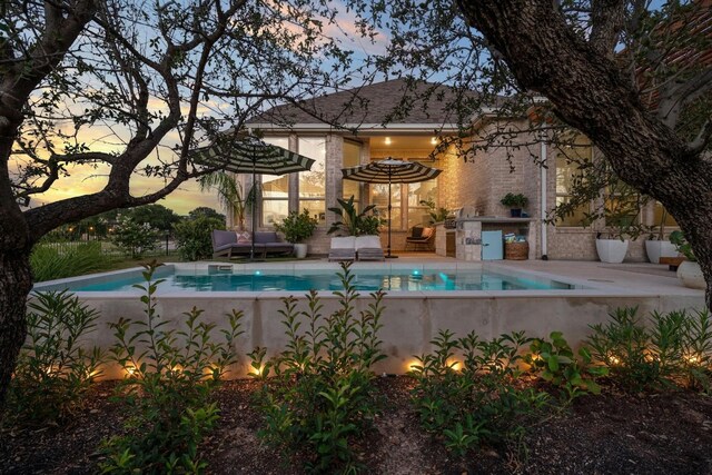 pool at dusk featuring a patio and area for grilling