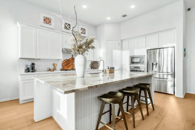 kitchen featuring stainless steel appliances, light hardwood / wood-style floors, light stone counters, an island with sink, and white cabinets