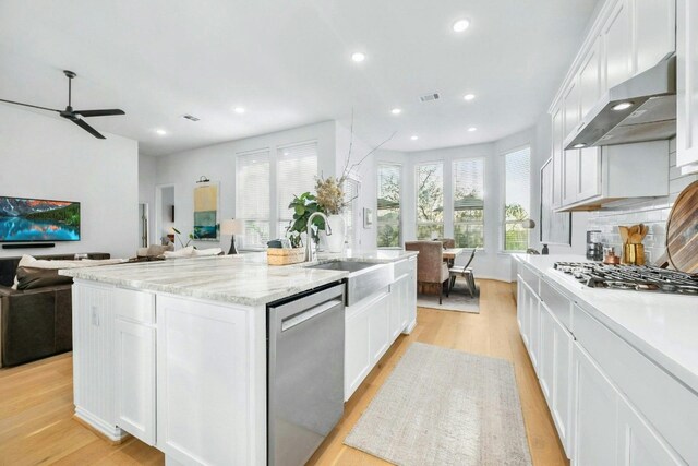 kitchen featuring a center island with sink, stainless steel appliances, exhaust hood, sink, and white cabinets