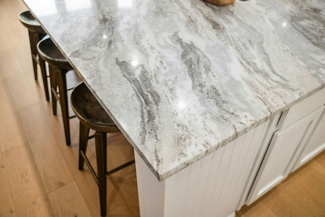 room details with light stone counters, indoor bar, a kitchen bar, and white cabinets