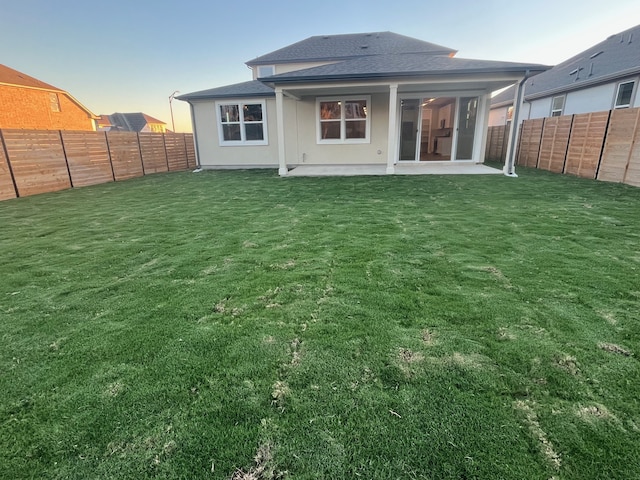 back house at dusk with a lawn and a patio