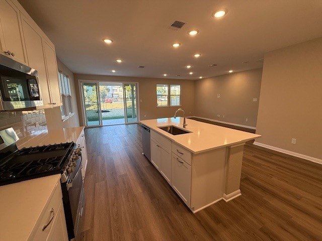 kitchen with dark hardwood / wood-style flooring, stainless steel appliances, sink, white cabinets, and an island with sink