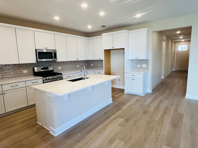 kitchen featuring sink, stainless steel appliances, a center island with sink, white cabinets, and light wood-type flooring