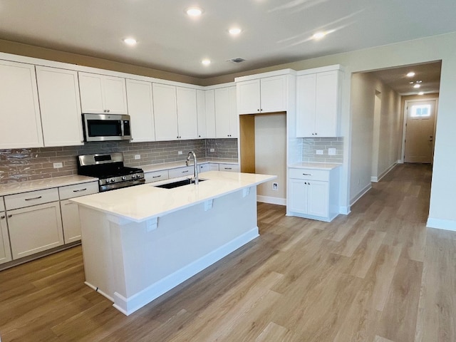 544 Raleigh Dr, Georgetown, TX 78633 - kitchen with stainless steel appliances, a sink, light wood-style flooring, decorative backsplash, and a center island with sink