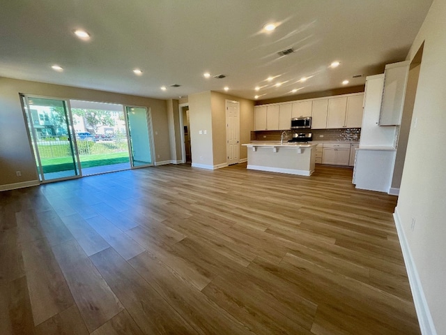 kitchen with stainless steel appliances, a kitchen island with sink, sink, light hardwood / wood-style floors, and white cabinetry