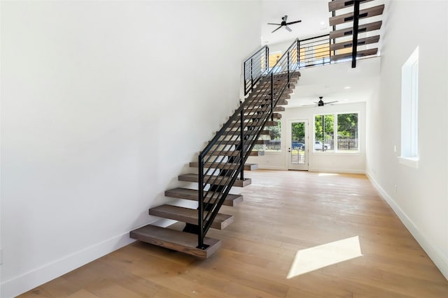 staircase with ceiling fan, a high ceiling, wood finished floors, and baseboards