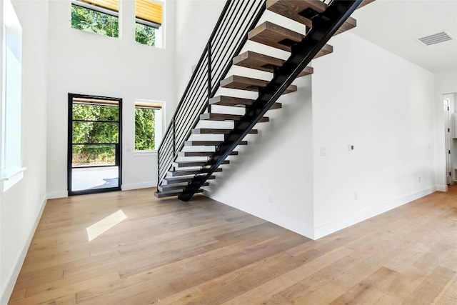 stairs with plenty of natural light, light wood-type flooring, and a towering ceiling