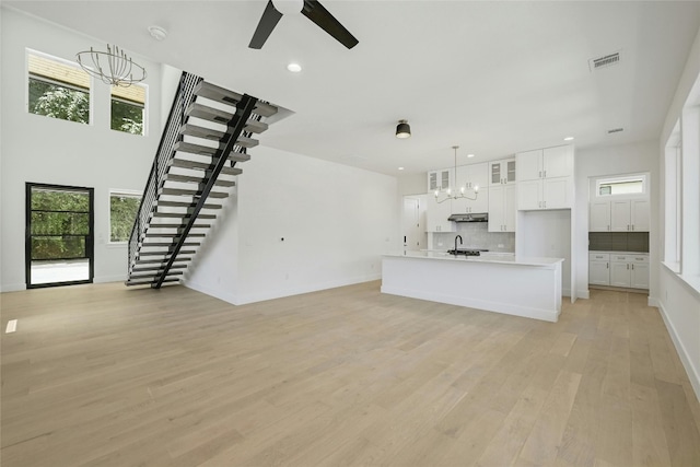 unfurnished living room featuring ceiling fan with notable chandelier, light hardwood / wood-style flooring, and a wealth of natural light