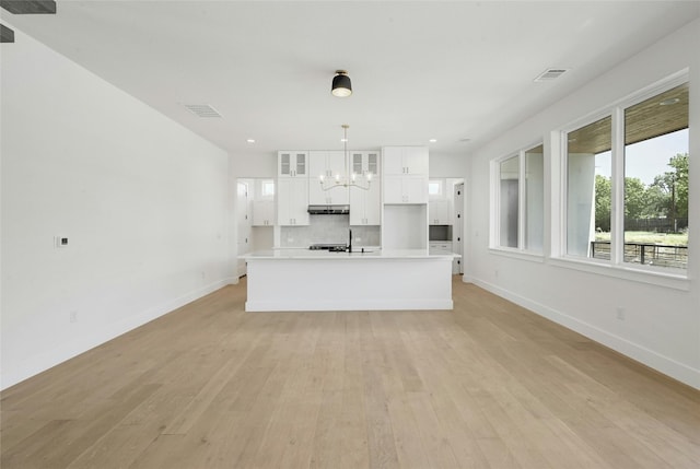 kitchen featuring light hardwood / wood-style floors, decorative backsplash, white cabinets, and an island with sink