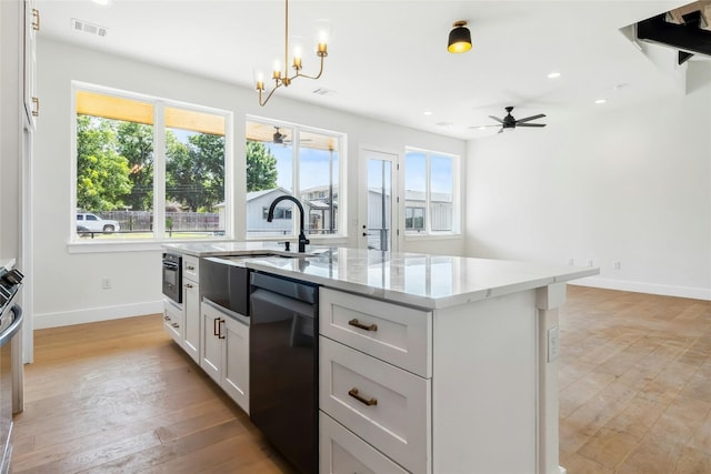 kitchen with black appliances, hanging light fixtures, a center island with sink, and plenty of natural light