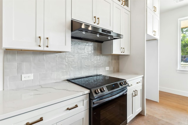 kitchen with light wood finished floors, black electric range oven, backsplash, light stone countertops, and under cabinet range hood