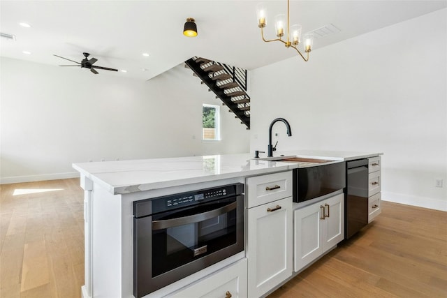 kitchen featuring white cabinetry, ceiling fan with notable chandelier, a kitchen island with sink, stainless steel appliances, and light hardwood / wood-style floors