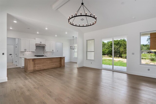 kitchen with decorative backsplash, hanging light fixtures, a kitchen island with sink, and light wood-type flooring