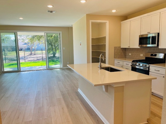 kitchen featuring stainless steel appliances, light hardwood / wood-style floors, a center island with sink, sink, and white cabinetry