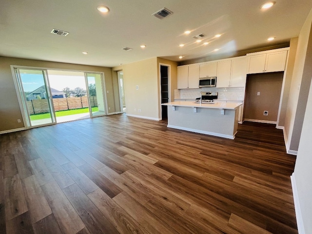 kitchen with stainless steel appliances, white cabinetry, an island with sink, and dark wood-type flooring