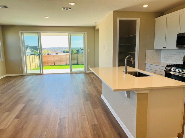 kitchen with stainless steel appliances, light hardwood / wood-style floors, sink, an island with sink, and white cabinets