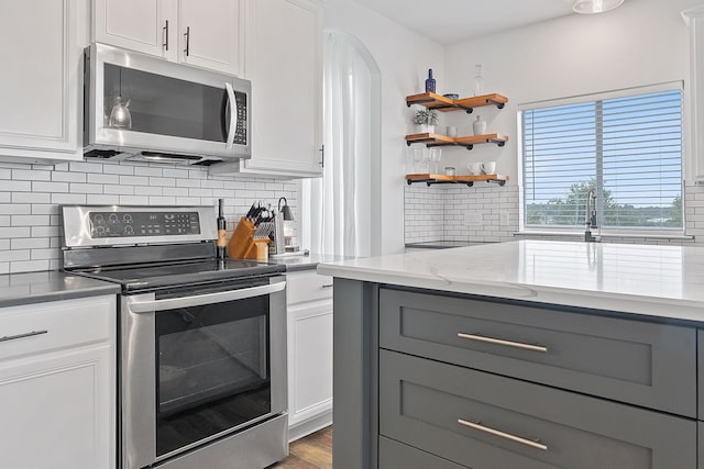 kitchen featuring appliances with stainless steel finishes, light hardwood / wood-style floors, light stone counters, white cabinetry, and backsplash