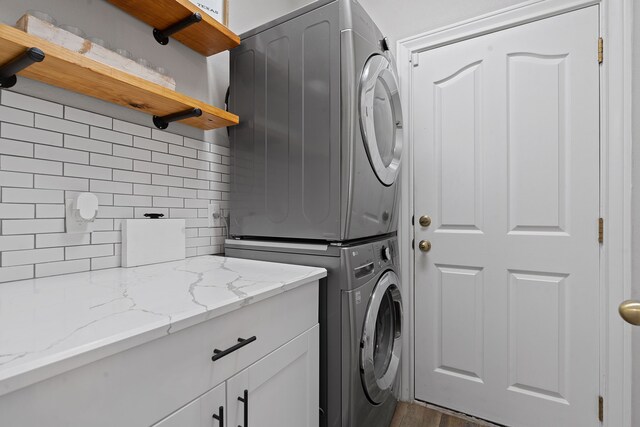 washroom with dark wood-type flooring, cabinets, and stacked washer and clothes dryer