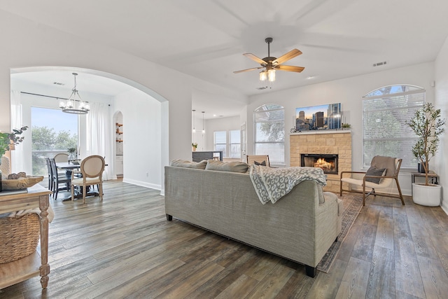 living room featuring hardwood / wood-style floors, ceiling fan with notable chandelier, a healthy amount of sunlight, and a stone fireplace