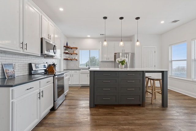 kitchen featuring white cabinets, a center island, hanging light fixtures, dark hardwood / wood-style flooring, and appliances with stainless steel finishes