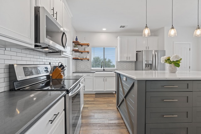 kitchen with sink, white cabinets, dark stone countertops, hanging light fixtures, and appliances with stainless steel finishes