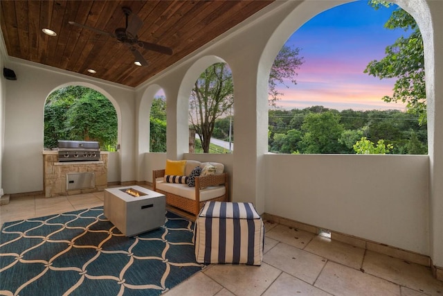 patio terrace at dusk with exterior kitchen, ceiling fan, grilling area, and a fire pit