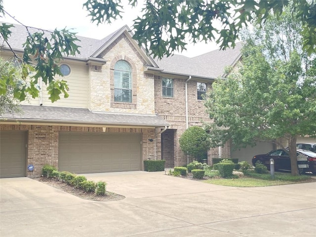 view of front of home with an attached garage, driveway, roof with shingles, and brick siding