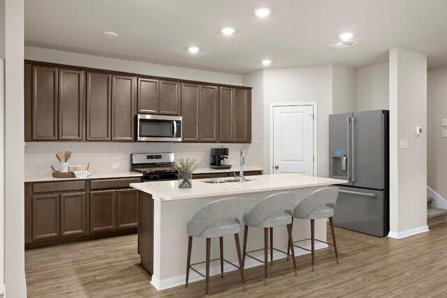 kitchen with appliances with stainless steel finishes, a kitchen island with sink, light hardwood / wood-style floors, and sink