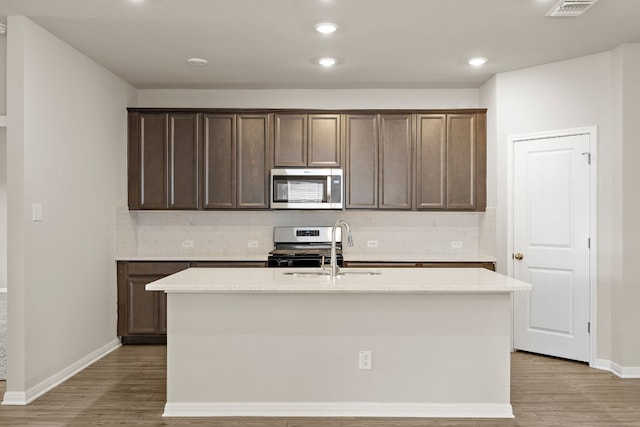 kitchen with backsplash, a center island with sink, light hardwood / wood-style floors, and stainless steel appliances